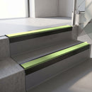 Square-edge aluminium stair nosing with a deep 56mm riser face in Satin Black, fitted along two vinyl-covered concrete steps in an office stairwell, with an Apple Green anti-slip PVC insert running the full width of each step