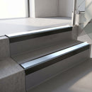 Square-edge aluminium stair nosing with a deep 56mm riser face in Satin Black, fitted along two vinyl-covered concrete steps in an office stairwell, with an Aura anti-slip PVC insert running the full width of each step