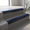 Square-edge aluminium stair nosing with a deep 56mm riser face in Satin Black, fitted along two vinyl-covered concrete steps in an office stairwell, with a Dark Blue anti-slip PVC insert running the full width of each step