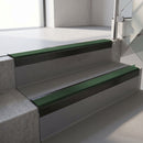 Square-edge aluminium stair nosing with a deep 56mm riser face in Satin Black, fitted along two vinyl-covered concrete steps in an office stairwell, with a Dark Green anti-slip PVC insert running the full width of each step