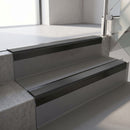 Square-edge aluminium stair nosing with a deep 56mm riser face in Satin Black, fitted along two vinyl-covered concrete steps in an office stairwell, with a Dark Grey anti-slip PVC insert running the full width of each step