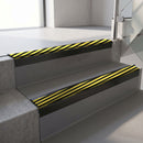 Square-edge aluminium stair nosing with a deep 56mm riser face in Satin Black, fitted along two vinyl-covered concrete steps in an office stairwell, with a Hazard anti-slip PVC insert running the full width of each step