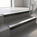 Square-edge aluminium stair nosing with a deep 56mm riser face in Satin Black, fitted along two vinyl-covered concrete steps in an office stairwell, with an Oyster anti-slip PVC insert running the full width of each step