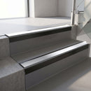 Square-edge aluminium stair nosing with a deep 56mm riser face in Satin Black, fitted along two vinyl-covered concrete steps in an office stairwell, with a Polar Grey anti-slip PVC insert running the full width of each step
