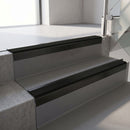 Square-edge aluminium stair nosing with a deep 56mm riser face in Satin Black, fitted along two vinyl-covered concrete steps in an office stairwell, with a Premium Black anti-slip PVC insert running the full width of each step