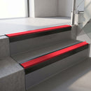 Square-edge aluminium stair nosing with a deep 56mm riser face in Satin Black, fitted along two vinyl-covered concrete steps in an office stairwell, with a Red anti-slip PVC insert running the full width of each step