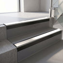 Square-edge aluminium stair nosing with a deep 56mm riser face in Satin Black, fitted along two vinyl-covered concrete steps in an office stairwell, with a White anti-slip PVC insert running the full width of each step