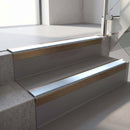 Square-edge aluminium stair nosing with a deep 56mm riser face in Satin Bronze, fitted along two vinyl-covered concrete steps in an office stairwell, with an Aura anti-slip PVC insert running the full width of each step