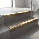Square-edge aluminium stair nosing with a deep 56mm riser face in Satin Bronze, fitted along two vinyl-covered concrete steps in an office stairwell, with a Beige anti-slip PVC insert running the full width of each step