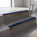 Square-edge aluminium stair nosing with a deep 56mm riser face in Satin Bronze, fitted along two vinyl-covered concrete steps in an office stairwell, with a Dark Blue anti-slip PVC insert running the full width of each step