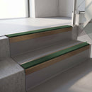 Square-edge aluminium stair nosing with a deep 56mm riser face in Satin Bronze, fitted along two vinyl-covered concrete steps in an office stairwell, with a Dark Green anti-slip PVC insert running the full width of each step