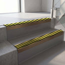 Square-edge aluminium stair nosing with a deep 56mm riser face in Satin Bronze, fitted along two vinyl-covered concrete steps in an office stairwell, with a Hazard anti-slip PVC insert running the full width of each step