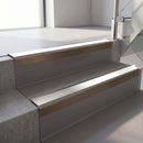 Square-edge aluminium stair nosing with a deep 56mm riser face in Satin Bronze, fitted along two vinyl-covered concrete steps in an office stairwell, with an Oyster anti-slip PVC insert running the full width of each step