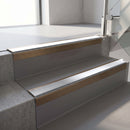 Square-edge aluminium stair nosing with a deep 56mm riser face in Satin Bronze, fitted along two vinyl-covered concrete steps in an office stairwell, with a Polar Grey anti-slip PVC insert running the full width of each step