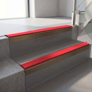 Square-edge aluminium stair nosing with a deep 56mm riser face in Satin Bronze, fitted along two vinyl-covered concrete steps in an office stairwell, with a Red anti-slip PVC insert running the full width of each step