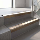 Square-edge aluminium stair nosing with a deep 56mm riser face in Satin Bronze, fitted along two vinyl-covered concrete steps in an office stairwell, with a Sahara anti-slip PVC insert running the full width of each step