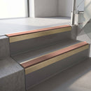 Square-edge aluminium stair nosing with a deep 56mm riser face in Satin Gold, fitted along two vinyl-covered concrete steps in an office stairwell, with a Mid Brown anti-slip PVC insert running the full width of each step