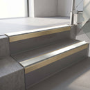 Square-edge aluminium stair nosing with a deep 56mm riser face in Satin Gold, fitted along two vinyl-covered concrete steps in an office stairwell, with an Oyster anti-slip PVC insert running the full width of each step