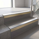 Square-edge aluminium stair nosing with a deep 56mm riser face in Satin Gold, fitted along two vinyl-covered concrete steps in an office stairwell, with a Polar Grey anti-slip PVC insert running the full width of each step