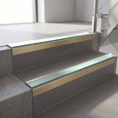 Square-edge aluminium stair nosing with a deep 56mm riser face in Satin Gold, fitted along two vinyl-covered concrete steps in an office stairwell, with a Sage Green anti-slip PVC insert running the full width of each step