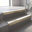 Square-edge aluminium stair nosing with a deep 56mm riser face in Satin Gold, fitted along two vinyl-covered concrete steps in an office stairwell, with a White anti-slip PVC insert running the full width of each step