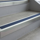Bright Polished deep-riser square-edge aluminium stair nosing fitted along two bare concrete steps, 62mm tread plate and 56mm front face, with a Blue anti-slip insert running the full width of each step