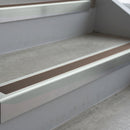Bright Polished deep-riser square-edge aluminium stair nosing fitted along two bare concrete steps, 62mm tread plate and 56mm front face, with a Brown anti-slip insert running the full width of each step