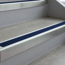 Bright Polished deep-riser square-edge aluminium stair nosing fitted along two bare concrete steps, 62mm tread plate and 56mm front face, with a Dark Blue anti-slip insert running the full width of each step