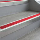 Bright Polished deep-riser square-edge aluminium stair nosing fitted along two bare concrete steps, 62mm tread plate and 56mm front face, with a Red anti-slip insert running the full width of each step