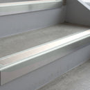 Bright Polished deep-riser square-edge aluminium stair nosing fitted along two bare concrete steps, 62mm tread plate and 56mm front face, with a White anti-slip insert running the full width of each step