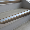 Dark Bronze deep-riser square-edge aluminium stair nosing fitted along two bare concrete steps, 62mm tread plate and 56mm front face, with a Aura anti-slip insert running the full width of each step
