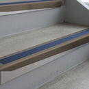 Dark Bronze deep-riser square-edge aluminium stair nosing fitted along two bare concrete steps, 62mm tread plate and 56mm front face, with a Blue anti-slip insert running the full width of each step