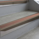 Dark Bronze deep-riser square-edge aluminium stair nosing fitted along two bare concrete steps, 62mm tread plate and 56mm front face, with a Mid Brown anti-slip insert running the full width of each step