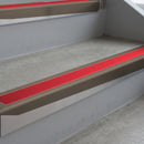 Dark Bronze deep-riser square-edge aluminium stair nosing fitted along two bare concrete steps, 62mm tread plate and 56mm front face, with a Red anti-slip insert running the full width of each step