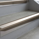 Dark Bronze deep-riser square-edge aluminium stair nosing fitted along two bare concrete steps, 62mm tread plate and 56mm front face, with a White anti-slip insert running the full width of each step