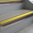 Dark Bronze deep-riser square-edge aluminium stair nosing fitted along two bare concrete steps, 62mm tread plate and 56mm front face, with a Yellow anti-slip insert running the full width of each step