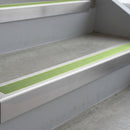 Mill Finish deep-riser square-edge aluminium stair nosing fitted along two bare concrete steps, 62mm tread plate and 56mm front face, with a Apple Green anti-slip insert running the full width of each step