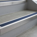 Mill Finish deep-riser square-edge aluminium stair nosing fitted along two bare concrete steps, 62mm tread plate and 56mm front face, with a Blue anti-slip insert running the full width of each step