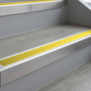 Mill Finish deep-riser square-edge aluminium stair nosing fitted along two bare concrete steps, 62mm tread plate and 56mm front face, with a Yellow anti-slip insert running the full width of each step