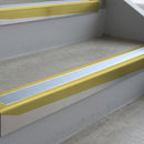 Mirrorflect Gold deep-riser square-edge aluminium stair nosing fitted along two bare concrete steps, 62mm tread plate and 56mm front face, with a Aura anti-slip insert running the full width of each step