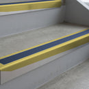 Mirrorflect Gold deep-riser square-edge aluminium stair nosing fitted along two bare concrete steps, 62mm tread plate and 56mm front face, with a Blue anti-slip insert running the full width of each step