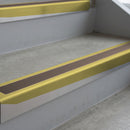 Mirrorflect Gold deep-riser square-edge aluminium stair nosing fitted along two bare concrete steps, 62mm tread plate and 56mm front face, with a Brown anti-slip insert running the full width of each step