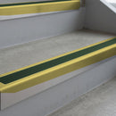 Mirrorflect Gold deep-riser square-edge aluminium stair nosing fitted along two bare concrete steps, 62mm tread plate and 56mm front face, with a Dark Green anti-slip insert running the full width of each step