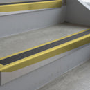 Mirrorflect Gold deep-riser square-edge aluminium stair nosing fitted along two bare concrete steps, 62mm tread plate and 56mm front face, with a Dark Grey anti-slip insert running the full width of each step