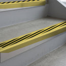 Mirrorflect Gold deep-riser square-edge aluminium stair nosing fitted along two bare concrete steps, 62mm tread plate and 56mm front face, with a Hazard anti-slip insert running the full width of each step