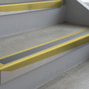 Mirrorflect Gold deep-riser square-edge aluminium stair nosing fitted along two bare concrete steps, 62mm tread plate and 56mm front face, with a Mid Grey anti-slip insert running the full width of each step