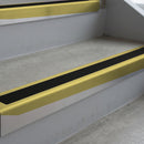 Mirrorflect Gold deep-riser square-edge aluminium stair nosing fitted along two bare concrete steps, 62mm tread plate and 56mm front face, with a Premium Black anti-slip insert running the full width of each step