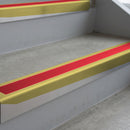 Mirrorflect Gold deep-riser square-edge aluminium stair nosing fitted along two bare concrete steps, 62mm tread plate and 56mm front face, with a Red anti-slip insert running the full width of each step