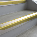 Mirrorflect Gold deep-riser square-edge aluminium stair nosing fitted along two bare concrete steps, 62mm tread plate and 56mm front face, with a White anti-slip insert running the full width of each step