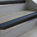 Satin Black deep-riser square-edge aluminium stair nosing fitted along two bare concrete steps, 62mm tread plate and 56mm front face, with a Blue anti-slip insert running the full width of each step